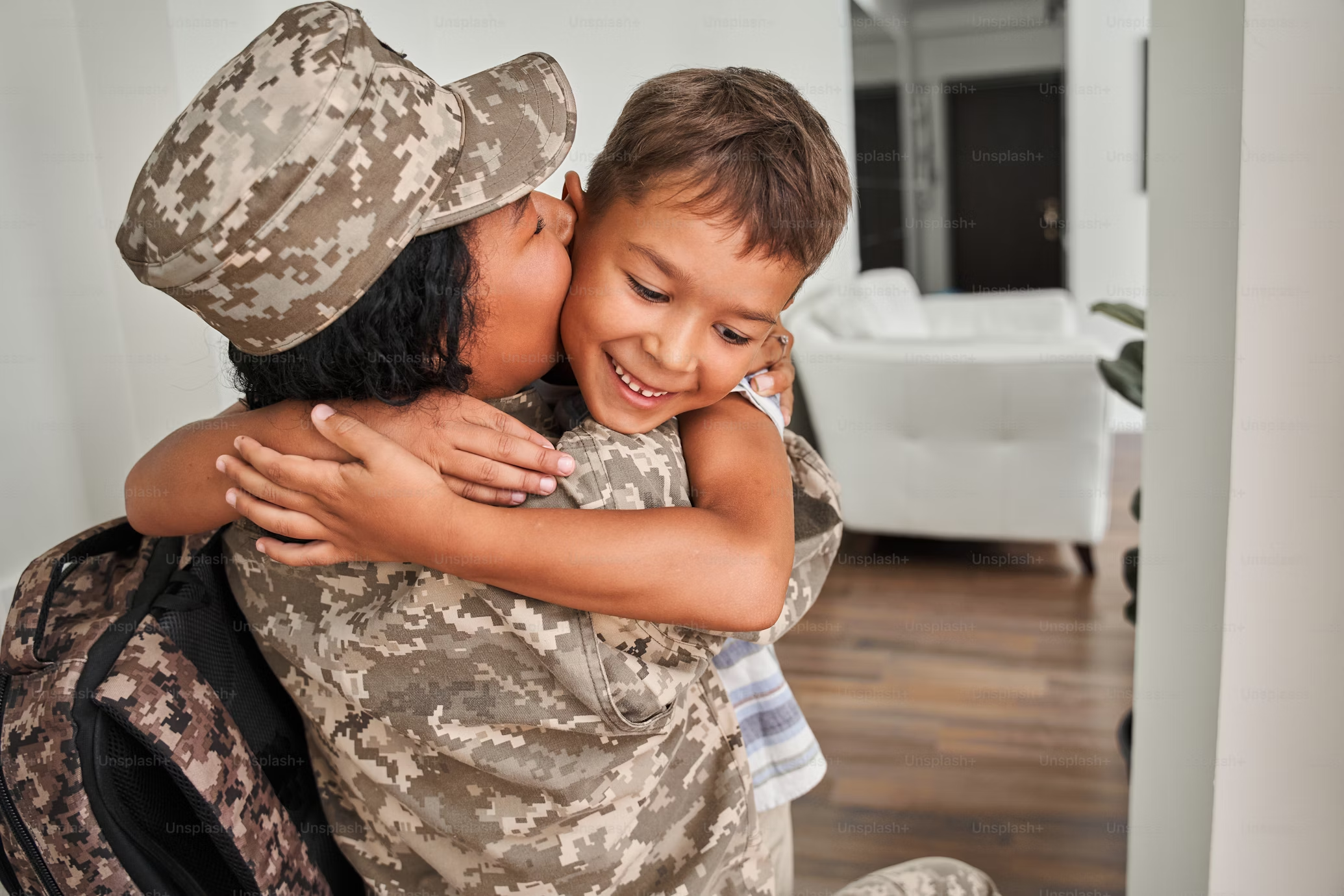 Military woman in her uniform hugs her young son, who is smiling brightly.